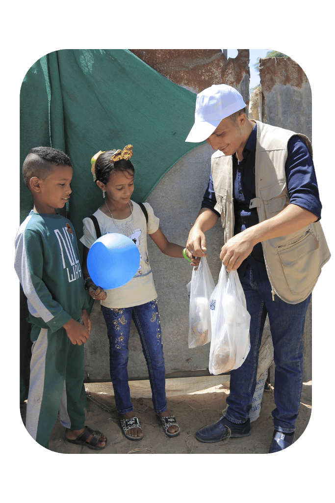 Ein humanitärer Helfer überreicht eine Tüte mit Adak-Fleisch an zwei palästinensische Kinder.