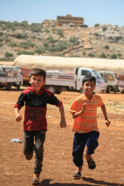 Zwei Jungen rennen fröhlich in einem syrischen Flüchtlingslager um die Wette.