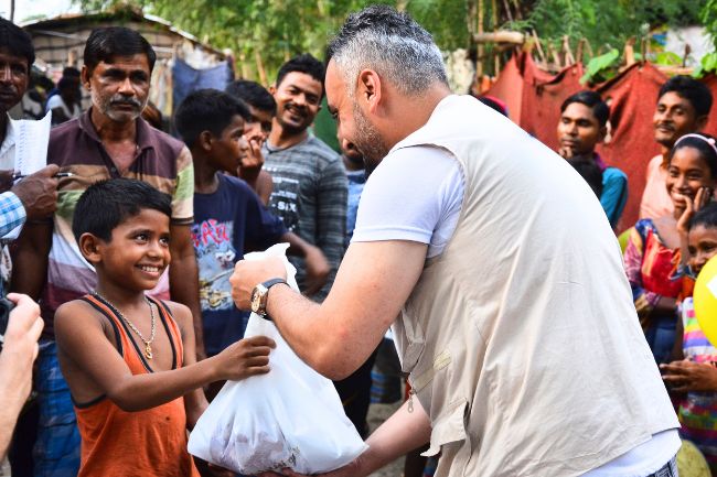 Ein humanitärer Helfer überreicht eine Tüte Kurbanfleisch an einen fröhlich schauenden Jungen in Bangladesch.