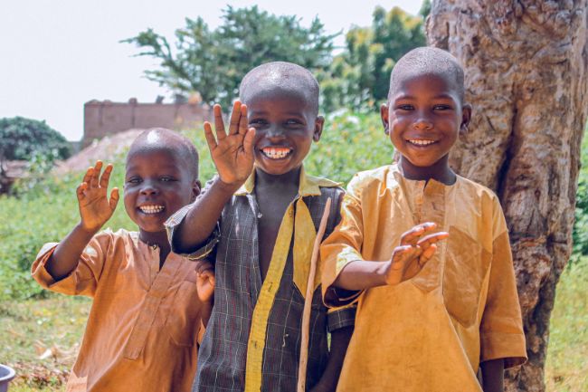 Drei Kinder in Festkleidung lächeln und winken. Traditionell erhalten Kinder am Opferfest ein Eid-Geschenk.