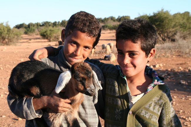 Zwei Jungen in Marokko tragen eine junge Ziege auf dem Arm.